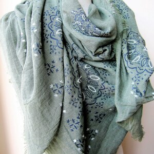 May include: A green scarf with a white and blue paisley pattern. The scarf is made of a soft, lightweight fabric and has a fringed edge.