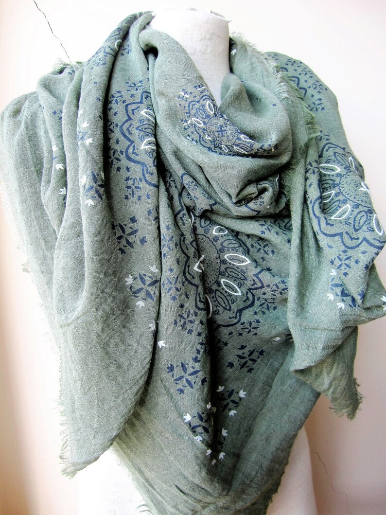 May include: A green scarf with a white and blue paisley pattern. The scarf is made of a soft, lightweight fabric and has a fringed edge.