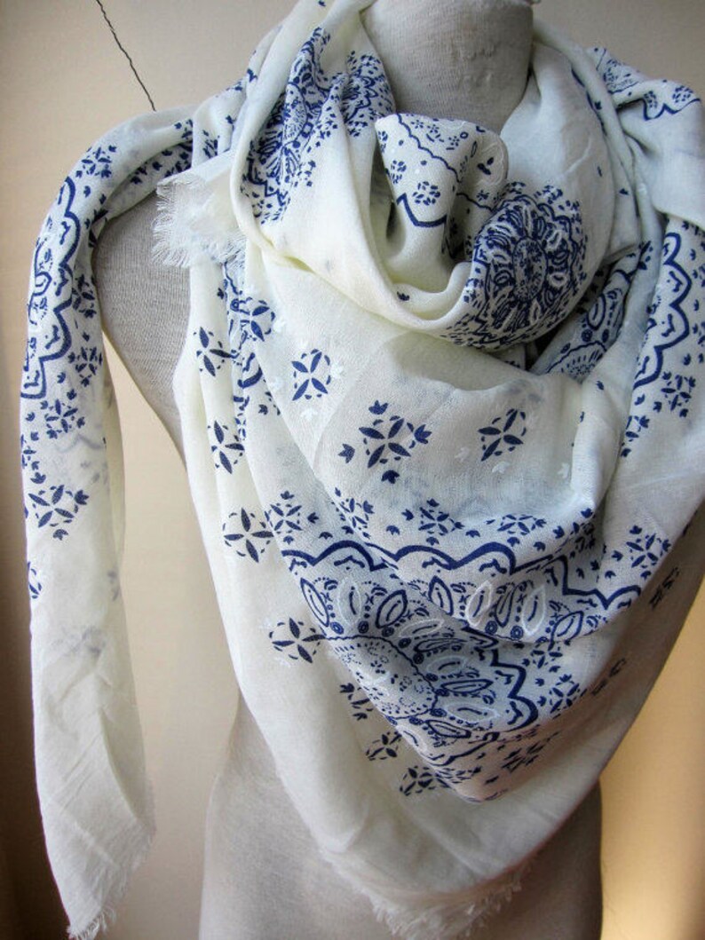 May include: White scarf with a blue paisley pattern. The scarf is made of a soft, lightweight fabric and has a fringed edge.