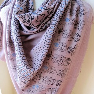 May include: A soft, pink cotton scarf with a black and blue paisley print. The scarf is folded and draped over a mannequin.