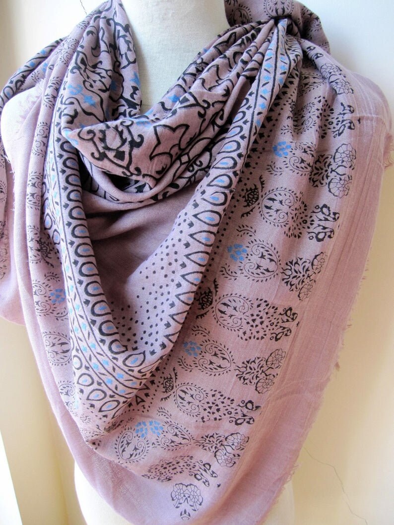 May include: A soft, pink cotton scarf with a black and blue paisley print. The scarf is folded and draped over a mannequin.