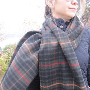 May include: A black and green plaid scarf with red and orange accents. The scarf is wrapped around a person's neck and is worn over a black quilted jacket.
