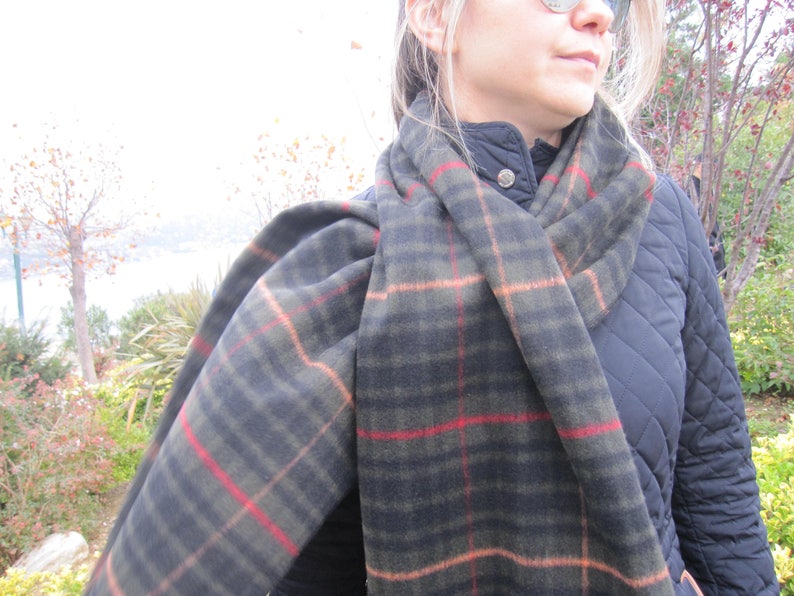 May include: A black and green plaid scarf with red and orange accents. The scarf is wrapped around a person's neck and is worn over a black quilted jacket.