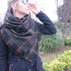 May include: A woman wearing a black quilted jacket with a large black and brown plaid scarf with fringe. The scarf is wrapped around her neck and shoulders.