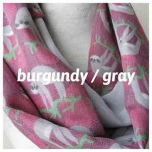 May include: Burgundy and gray infinity scarf with a sloth print. The scarf is made of a soft, comfortable fabric and features a repeating pattern of sloths hanging from branches.