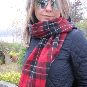 May include: A woman wearing a navy blue quilted jacket with a red and black plaid scarf. She is wearing sunglasses and has long blonde hair.