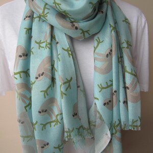 May include: A light blue scarf with a pattern of sloths hanging from branches. The sloths are gray and the branches are green.