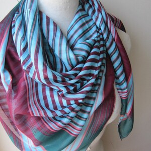 May include: A striped scarf in shades of teal, blue, pink, and burgundy. The scarf is made of a lightweight fabric and is perfect for adding a pop of color to any outfit.