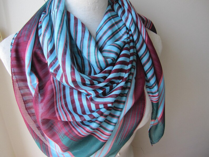 May include: A striped scarf in shades of teal, blue, pink, and burgundy. The scarf is made of a lightweight fabric and is perfect for adding a pop of color to any outfit.