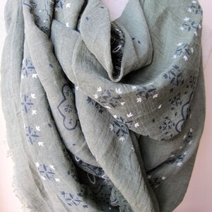 May include: A green scarf with a white and blue paisley pattern. The scarf is made of a soft, lightweight fabric and has a fringed edge.