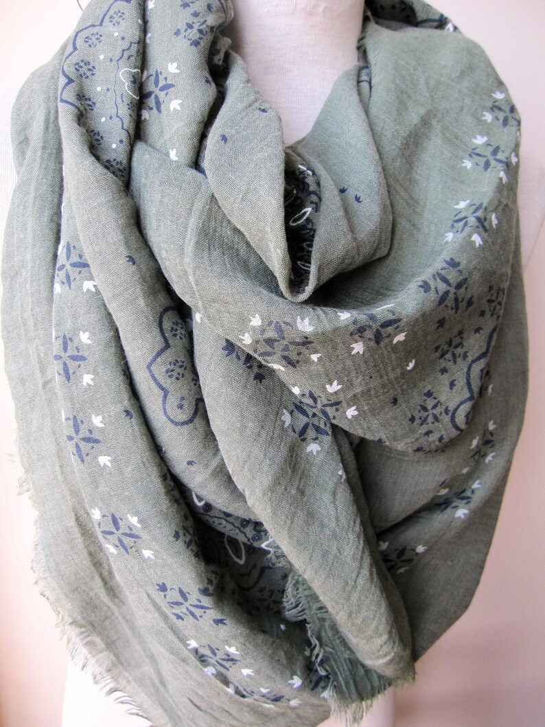 May include: A green scarf with a white and blue paisley pattern. The scarf is made of a soft, lightweight fabric and has a fringed edge.