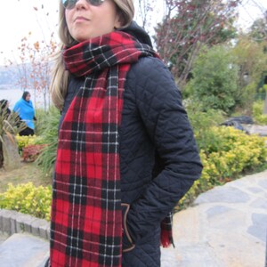 May include: A woman wearing a black quilted jacket with a red and black plaid scarf. She is wearing sunglasses and has her hair pulled back.