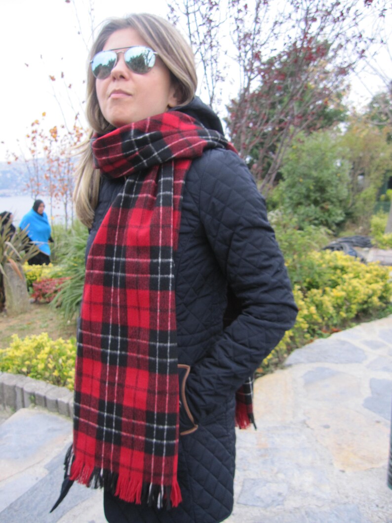 May include: A woman wearing a black quilted jacket with a red and black plaid scarf. She is wearing sunglasses and has her hair pulled back.