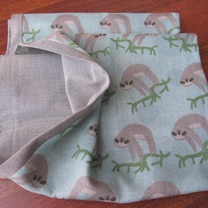 May include: A blue and gray fabric with a pattern of sloths on branches. The fabric is folded in half and has a textured surface.