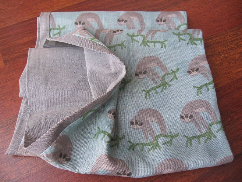 May include: A blue and gray fabric with a pattern of sloths on branches. The fabric is folded in half and has a textured surface.