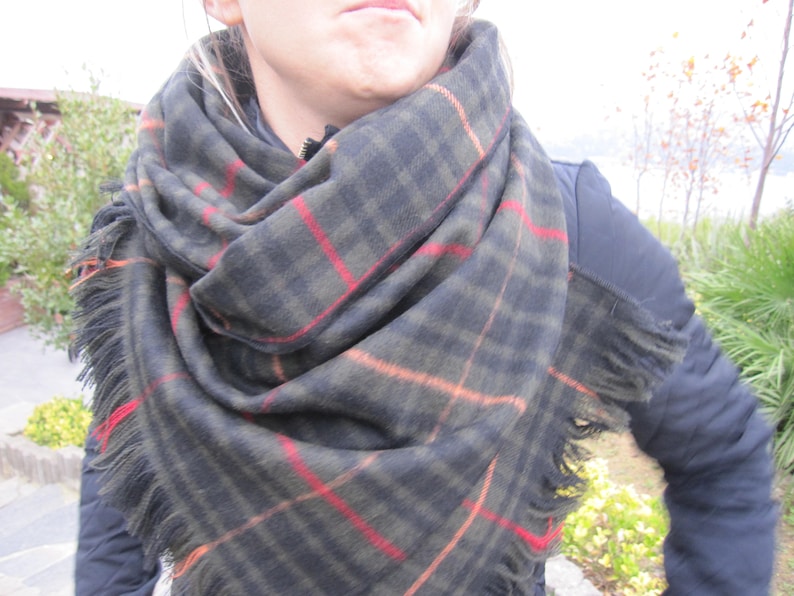 May include: A black and green plaid scarf with fringed edges. The scarf is folded and draped around a person's neck.