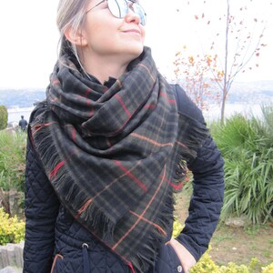 May include: A woman wearing a black quilted jacket with a brown trim and a black and green plaid scarf with fringe. She is wearing mirrored sunglasses and looking up.
