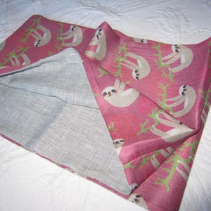 May include: A pink fabric pillowcase with a white sloth pattern. The pillowcase is folded in half, showing the inside of the fabric, which is a light gray.