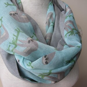 May include: A light blue and gray infinity scarf with a pattern of sloths hanging from branches. The scarf is made of a soft, comfortable fabric and is perfect for keeping warm in the winter.
