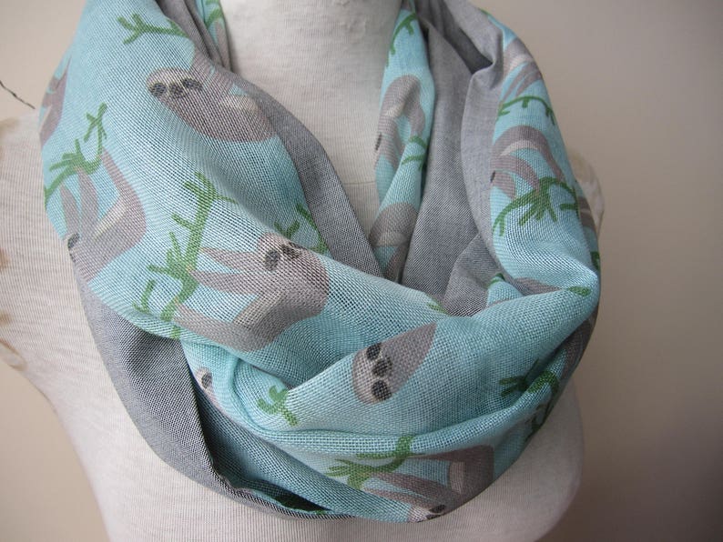 May include: A light blue and gray infinity scarf with a pattern of sloths hanging from branches. The scarf is made of a soft, comfortable fabric and is perfect for keeping warm in the winter.