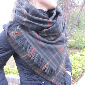 May include: A black and green plaid scarf with orange and red accents. The scarf has fringe on the edges.