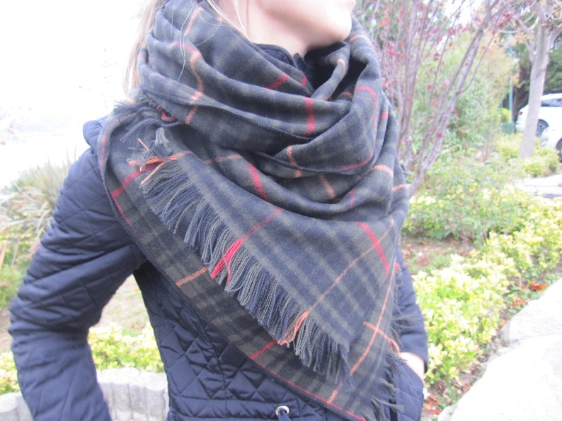 May include: A black and green plaid scarf with orange and red accents. The scarf has fringe on the edges.