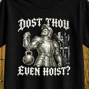 Könnte beinhalten: Ein schwarzes Kurzarm-T-Shirt mit einer weißen Grafik eines Ritters in Rüstung, der eine Kettlebell hebt. Der Text über dem Ritter lautet DOST THOU und der Text darunter lautet EVEN HOIST? Das Design ist mittig auf der Vorderseite platziert.