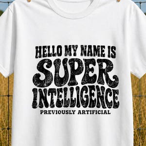 Peut inclure: Un t-shirt blanc à manches courtes avec un texte noir vieilli indiquant HELLO MY NAME IS SUPER INTELLIGENCE PREVIOUSLY ARTIFICIAL. Le t-shirt possède un col rond et est suspendu par deux pinces à linge en bois sur une clôture en fil de fer.
