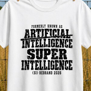 Può includere: Una t-shirt bianca a maniche corte con testo nero in stile usurato che recita: FORMERLY KNOWN AS ARTIFICIAL INTELLIGENCE SUPER INTELLIGENCE (SI) REBRAND 2026. Il capo presenta un girocollo e una vestibilità standard su sfondo bianco.