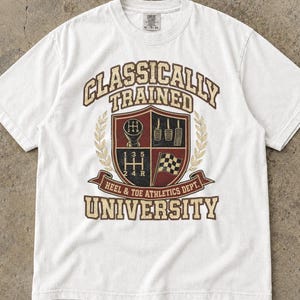 Puede incluir: Una camiseta blanca de manga corta con un estampado gráfico con el texto Classically Trained University y Heel & Toe Athletics Dept. El diseño incluye un escudo con una palanca de cambios, pedales y una bandera a cuadros en rojo y marrón.