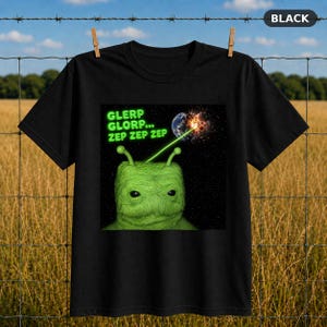 Op de afbeelding: Een zwart t-shirt met een afbeelding van een pluizig groen buitenaards wezen met twee antennes. Het wezen schiet een groene laserstraal naar een planeet in de ruimte. De tekst GLERP GLORP... ZEP ZEP ZEP staat in felgroene letters boven het hoofd.