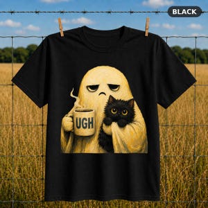 Könnte beinhalten: Ein schwarzes T-Shirt mit einer Grafik eines blassgelben Geistes mit mürrischem Gesichtsausdruck, der eine beige Tasse mit dem aufgedruckten Text UGH hält. Der Geist hält zudem eine flauschige schwarze Katze mit großen gelben Augen vor der Brust.