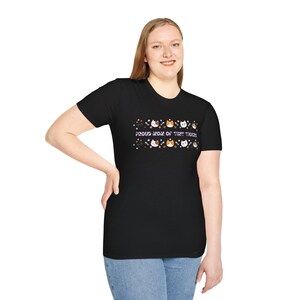 May include: Black t-shirt featuring the text "PROUD MOM OF TINY TIGERS" in white, with a row of cartoon cat faces. The cats have different colours and patterns. The woman is wearing blue jeans.
