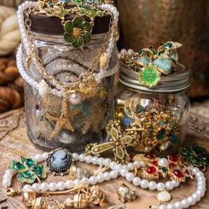 Pode incluir: Uma coleção de joias, incluindo colares, pulseiras e anéis, exibida em uma superfície de madeira. As joias apresentam pérolas, detalhes dourados e vários pingentes, incluindo estrelas do mar e conchas. Algumas peças são armazenadas em potes de vidro.