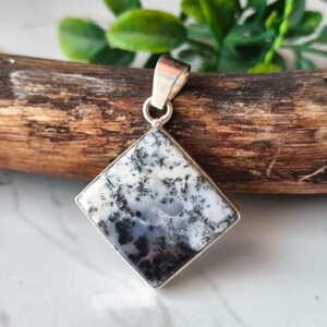 May include: A square pendant with a silver bail. The pendant features a dendritic agate stone with a pattern of black and gray inclusions on a white background. The stone is set in a silver bezel.