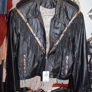 May include: Black leather jacket with fringe and a snake skin pattern trim. The jacket has a zipper closure and a tag that says "Vintage Leather Jacket".