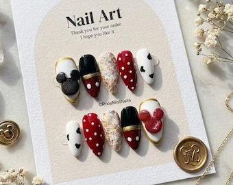 May include: A collection of ten artificial nails featuring diverse designs, such as polka dots, glitter, and Mickey Mouse motifs. The nails are presented on a card with the text "Nail Art" and "Thank you for your order. I hope you like it."