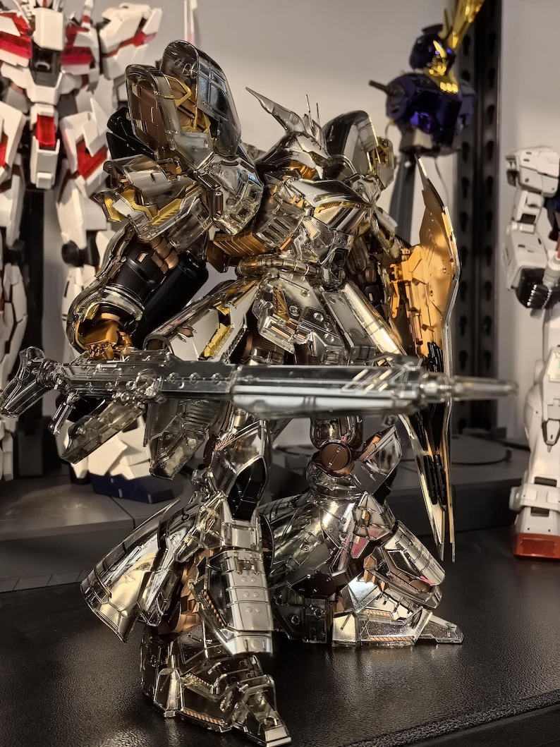 May include: A detailed, metallic silver and gold robot model with a large gun and shield. The robot has intricate armor plating and is posed in a dynamic stance. Other robot models are visible in the background, suggesting a collection of similar figures.