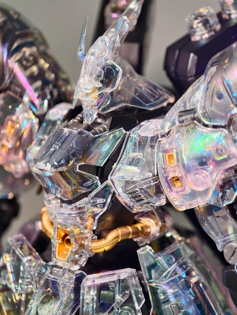 May include: Close-up of a clear, iridescent robot model. The model features intricate details, including a transparent head, chest, and arms. Gold-colored tubes and accents are visible. The robot's design suggests a futuristic or science fiction theme.