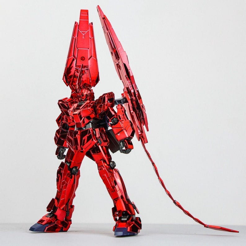 May include: A metallic red robot model with intricate details, featuring a large headpiece and a long, segmented tail. The robot is posed in a standing position, showcasing its angular design and reflective surface. The feet are dark blue.