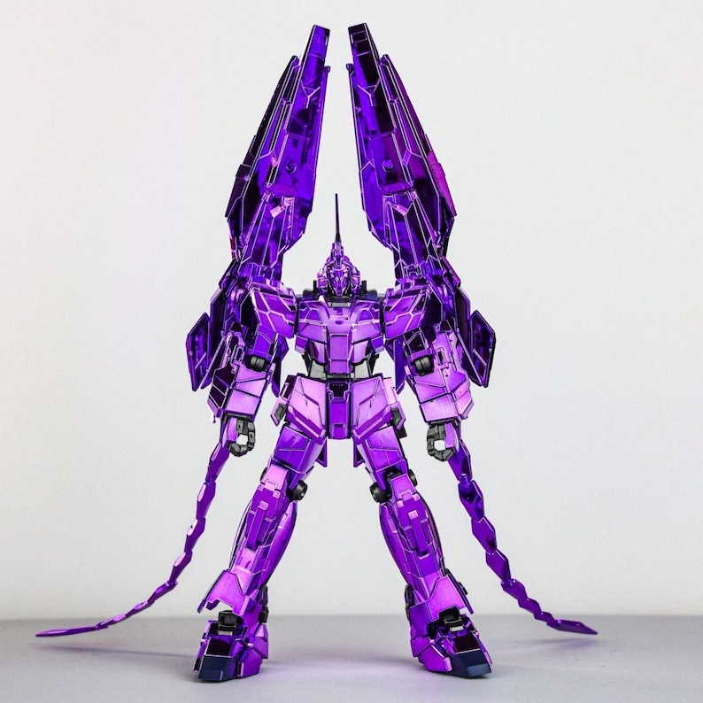 May include: A metallic purple robot figure with large, angular wings extending upwards. The robot has a detailed design with sharp edges and a long, tail-like appendage. The figure is standing on a flat surface against a plain background.