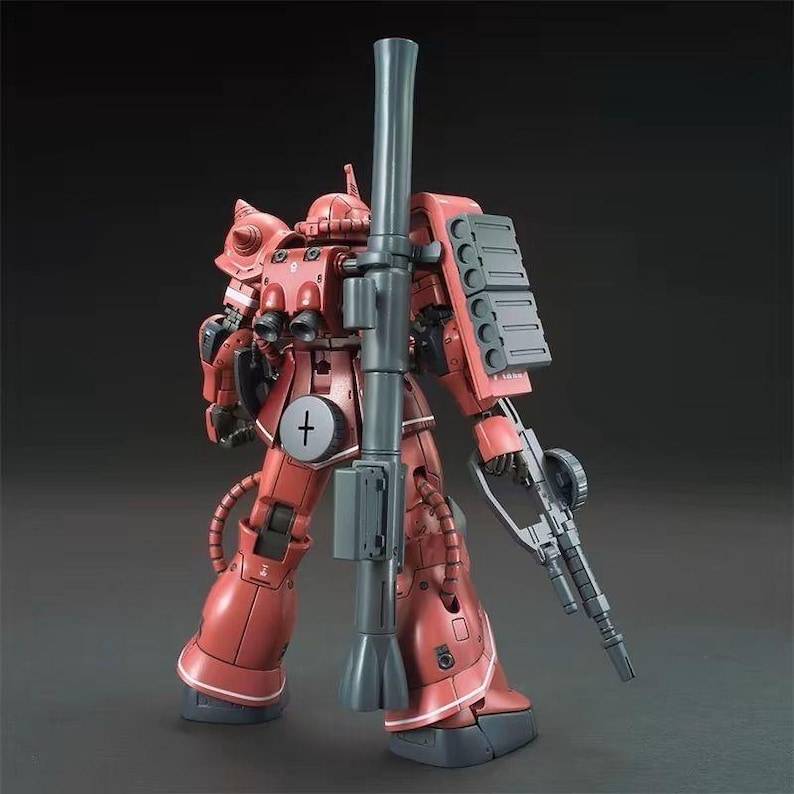 Puede incluir: Maqueta roja y gris de un traje m&oacute;vil, con un ca&ntilde;&oacute;n grande y un rifle. El modelo tiene componentes mec&aacute;nicos detallados y un s&iacute;mbolo de cruz en el pecho. El kit est&aacute; posado sobre un fondo oscuro.