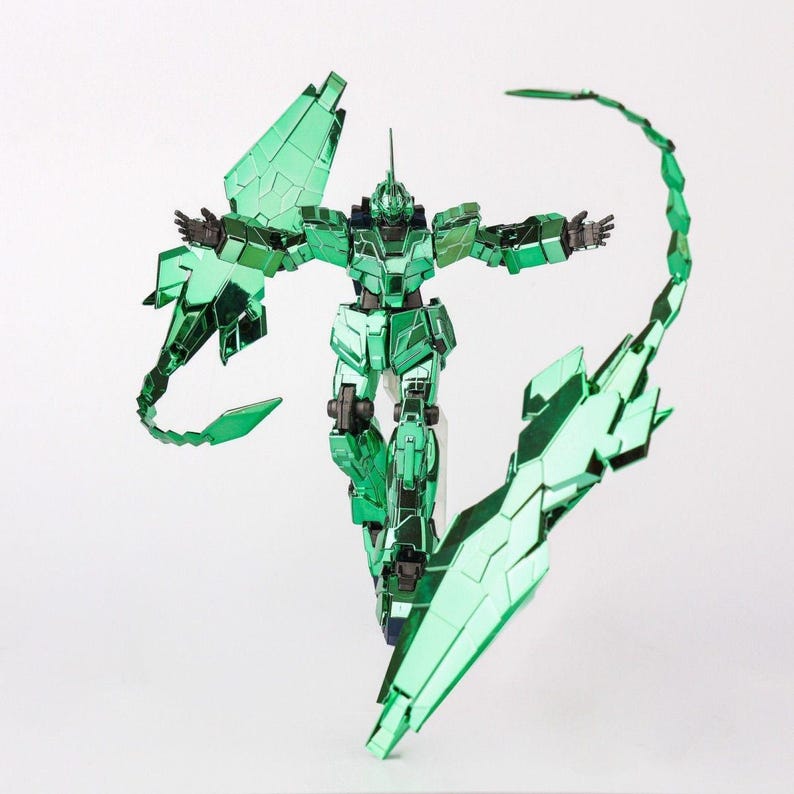 May include: A metallic green robot action figure with articulated limbs and intricate panel details. The figure has outstretched arms and is posed with large, segmented wing-like structures and a curved tail. The figure is standing on a clear stand.