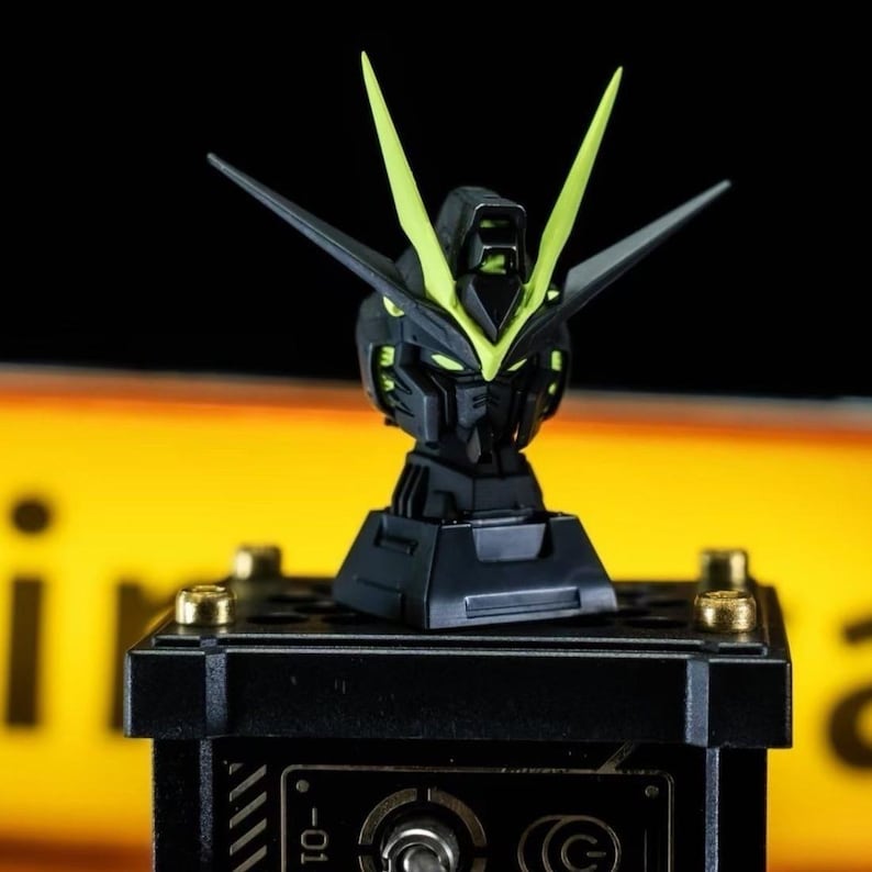 May include: A black and neon green Gundam model head, featuring sharp angles and a detailed design. The head is mounted on a black base with gold accents. The model has two prominent, upward-pointing neon green fins.
