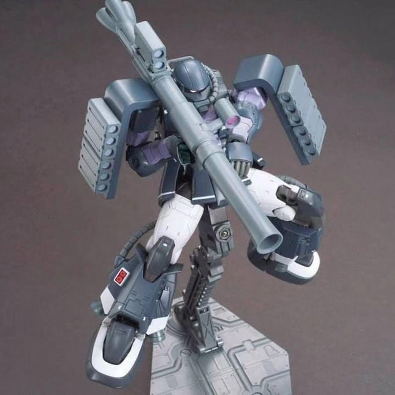 Puede incluir: Un modelo de robot gris y morado con un arma grande. El robot est&aacute; posicionado en una postura din&aacute;mica, con las piernas dobladas y los brazos extendidos. Tiene m&uacute;ltiples paneles grises y detalles en blanco. El modelo est&aacute; sobre una base gris.