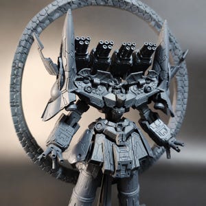 May include: A gray, detailed model of a robot with multiple cannons and a circular, textured frame. The robot has a complex design with multiple panels, spikes, and gun barrels. The model is a collectible item.