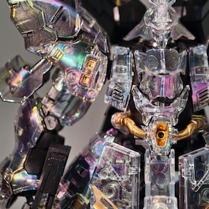 May include: A clear, iridescent robot model with intricate details. The robot features transparent armor, gold accents, and a complex internal structure. The design includes sharp angles and a futuristic aesthetic, showcasing a detailed and articulated figure.