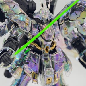 May include: A clear, iridescent robot model with a green laser sword. The model has intricate details, including gold accents and a black backpack. The robot's armor reflects a rainbow of colors.