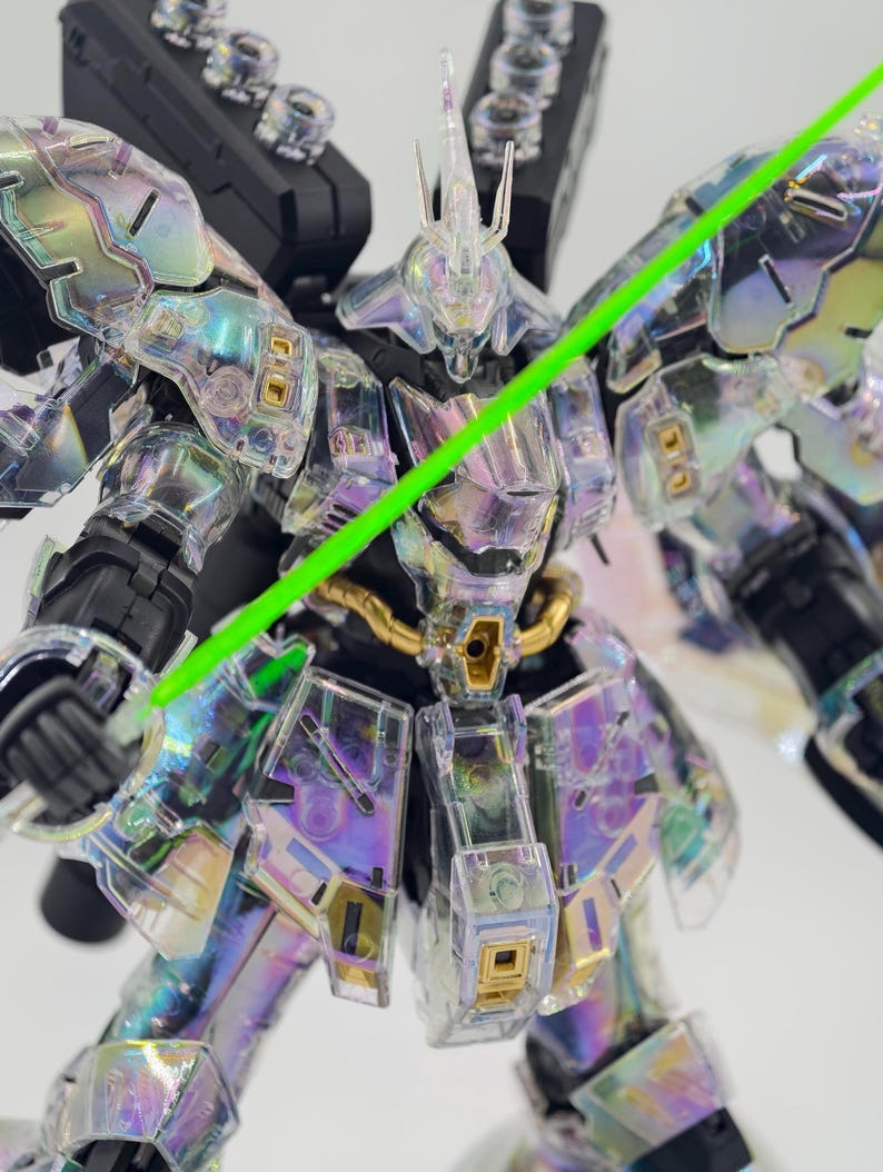 May include: A clear, iridescent robot model with a green laser sword. The model has intricate details, including gold accents and a black backpack. The robot's armor reflects a rainbow of colors.