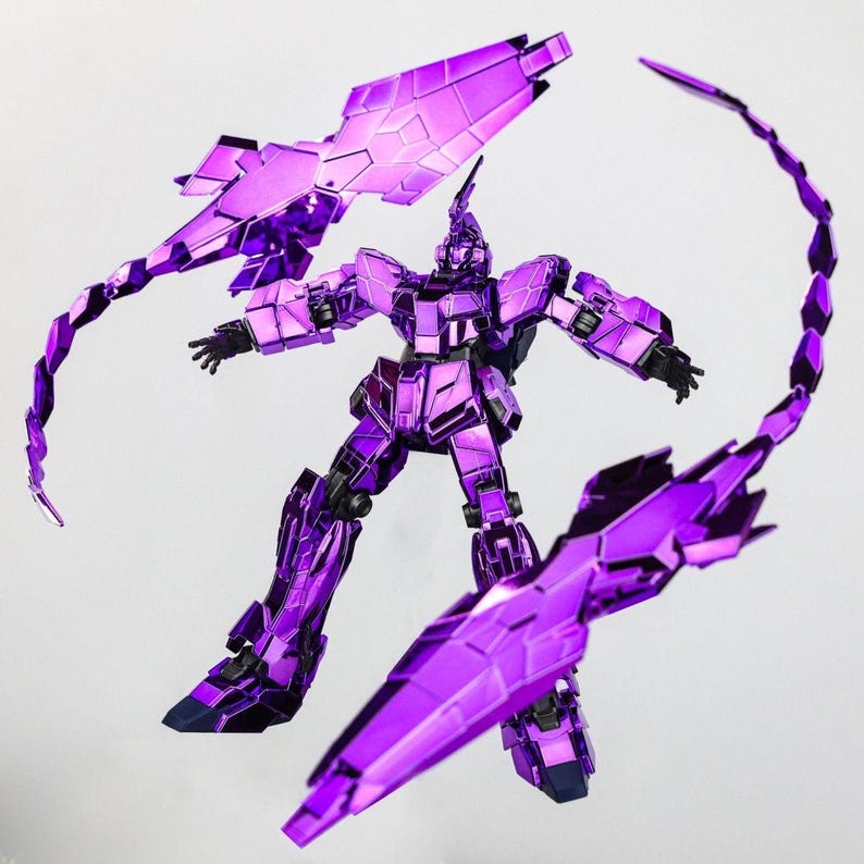 May include: A metallic purple robot action figure with articulated limbs and multiple weapon attachments. The figure is posed dynamically against a white background, showcasing its intricate design and reflective surface. The robot has a horn on its head.